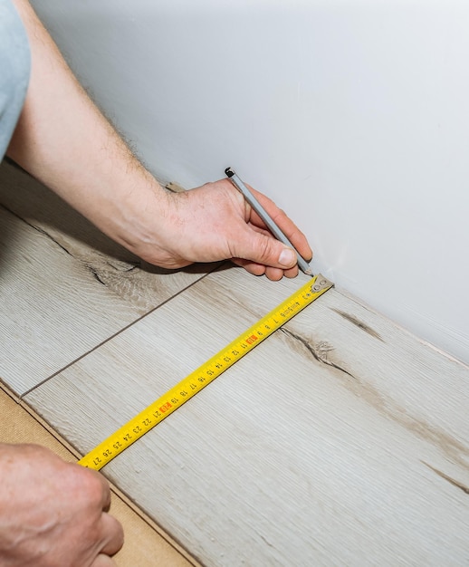 Lavoratore che fa pavimenti in laminato in appartamento Misura nastro e matita nelle mani Manutenzione, riparazione, ristrutturazione Assi di parquet in legno all'interno