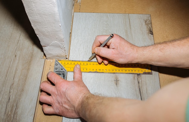 Lavoratore che fa pavimenti in laminato in appartamento Misura nastro e matita nelle mani Manutenzione, riparazione, ristrutturazione Assi di parquet in legno all'interno