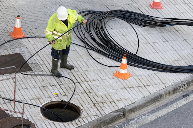 Lavoratore che maneggia un cavo di comunicazione sul marciapiede di una città