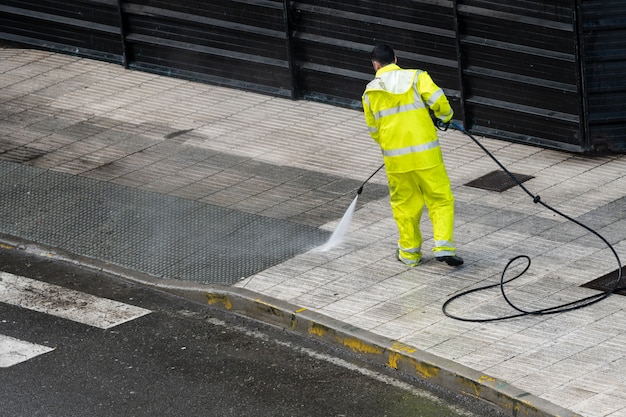 Lavoratore che pulisce il marciapiede con acqua in pressione. Concetto di manutenzione o pulizia