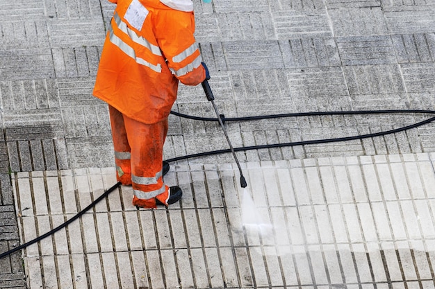 Lavoratore che pulisce un marciapiede stradale con getto d'acqua ad alta pressione Copia spazio