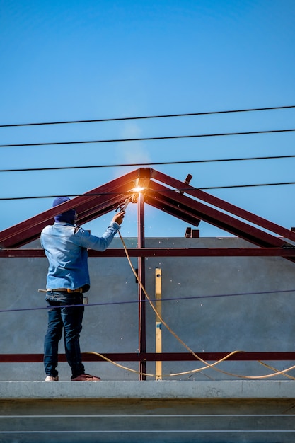 Lavoratore che sta sul tetto e sulla struttura della saldatura della casa nel cantiere