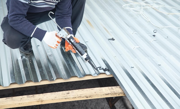 Lavoratore che utilizza una pistola per colla con adesivo per fissare l'acciaio metallico sul tetto