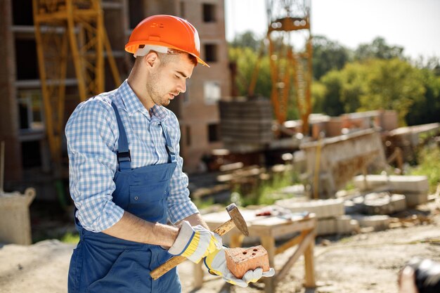 Lavoratore con casco arancione in un cantiere che tiene un martello e un mattone