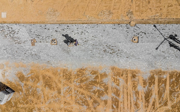 Lavoratore con compattatore a piastra vibrante che compatta sabbia sulla vista dall'alto del cantiere stradale o sul marciapiede