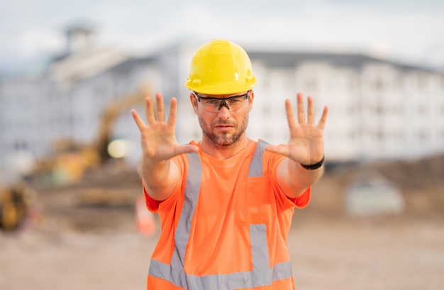 Lavoratore con il costruttore di gesto della mano di arresto in un elmetto che lavora a un progetto di costruzione in un sito a bu