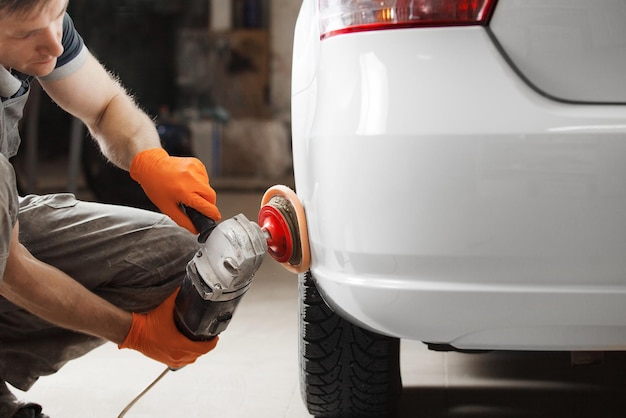 Lavoratore con lucidatrice orbitale in officina di riparazione auto Dettagli auto Recupero finale dell'automobile