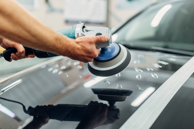 Lavoratore con lucidatrice pulisce il cofano dell'auto. Dettagli auto sul servizio di autolavaggio