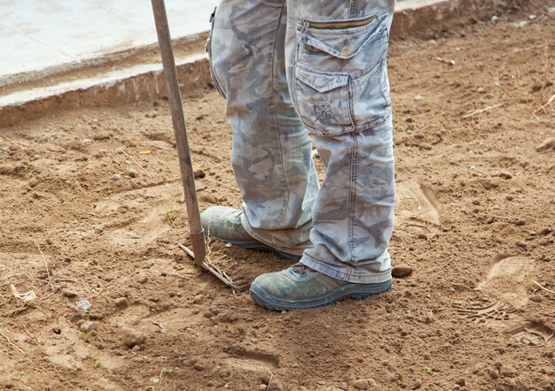 Lavoratore con rastrello mentre schiaccia il terreno nel cortile