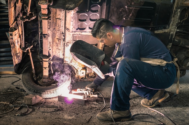 Lavoratore del meccanico del giovane che ripara il vecchio corpo d&#39;annata dell&#39;automobile in garage sudicio