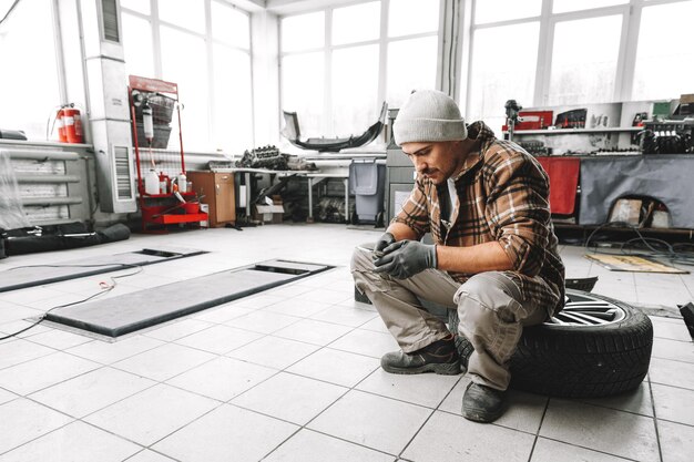Lavoratore del servizio auto seduto su una ruota e in riposo usando il telefono cellulare