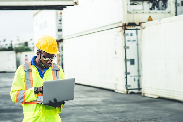 Lavoratore dell'Africa nera che lavora nella spedizione logistica utilizzando il computer portatile per controllare i contenitori di carico al carico portuale per il caposquadra delle merci di importazione e esportazione che guarda in alto per il futuro