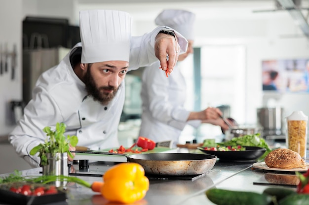 Lavoratore dell'industria alimentare che cucina delizioso piatto gourmet per il servizio di cena al ristorante. Chef esperto e sicuro di sé che trita il peperone rosso biologico e fresco mentre prepara la guarnizione.