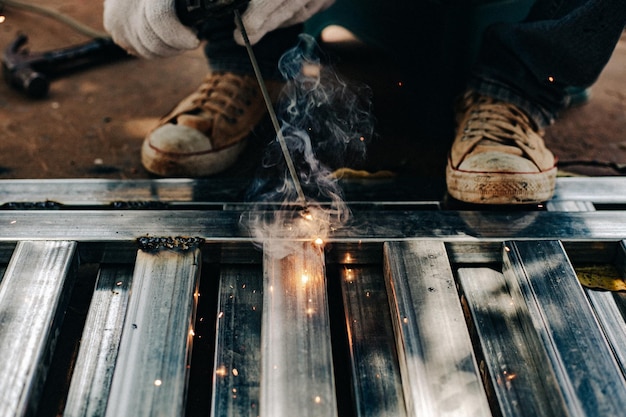 Lavoratore dell'industria che indossa guanti bianchi e ferro da saldatura al lavoro all'aperto Strumento manuale di primo piano per la saldatura dell'acciaio Concetto industriale che utilizza una macchina da saldatura per la costruzione