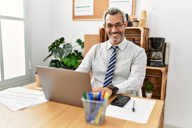 Lavoratore di affari dell'uomo dai capelli grigi di mezza età che utilizza il computer portatile che lavora all'ufficio