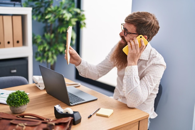 Lavoratore di affari dell'uomo della testarossa giovane che parla sul taccuino della lettura dello smartphone all'ufficio