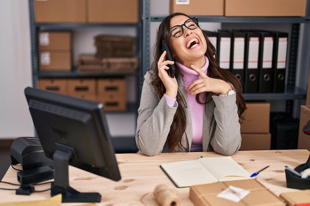 Lavoratore di affari di commercio elettronico della giovane donna ispanica che parla sullo smartphone all'ufficio