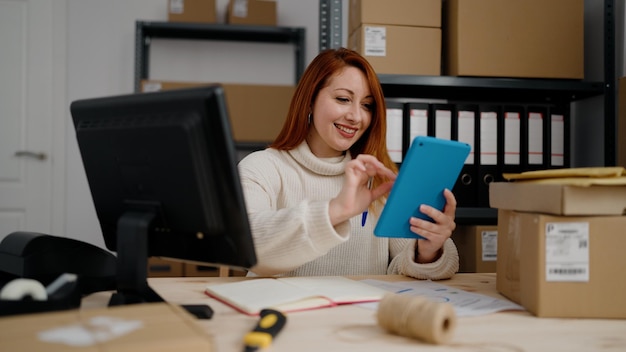 Lavoratore di affari di e-commerce di giovane donna rossa utilizzando il touchpad in ufficio