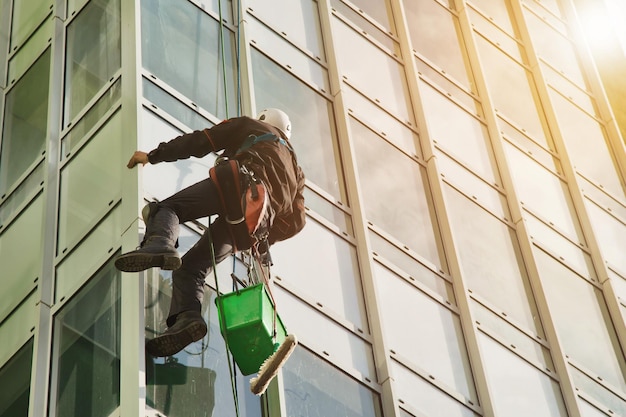 Lavoratore di alpinismo industriale nel lavaggio uniforme dei vetri esterni su un edificio di facciata residenziale