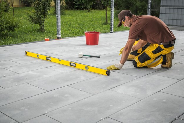 Lavoratore di costruzione caucasico che costruisce un moderno patio pavimento di piastrelle di cemento in un cortile residenziale