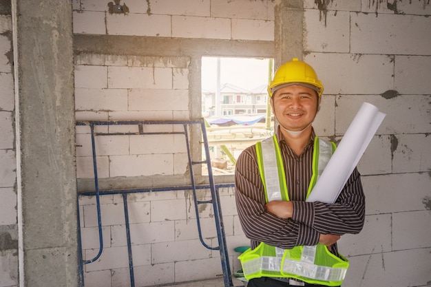 Lavoratore di ingegnere edile uomo d'affari asiatico in casco protettivo e carta cianografie a portata di mano al cantiere di casa