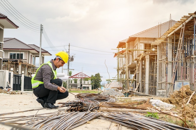 Lavoratore di ingegnere edile uomo d'affari asiatico in casco protettivo e carta cianografie a portata di mano guardando la barra d'acciaio al cantiere di casa