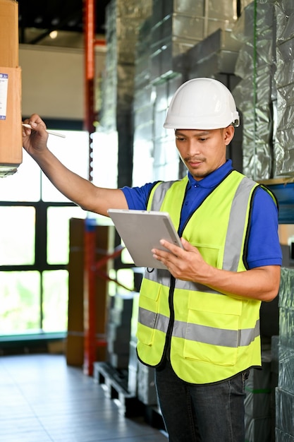 Lavoratore di magazzino maschio asiatico concentrato che utilizza il tablet per controllare e gestire il suo inventario