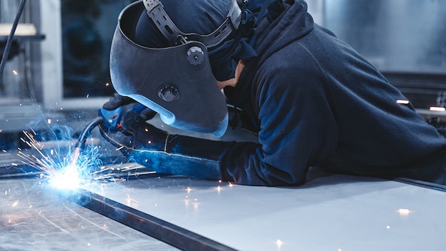 lavoratore di sesso maschile che indossa casco e guanti per saldare la costruzione in acciaio in fabbrica