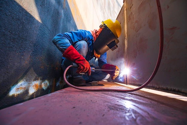 Lavoratore di sesso maschile che indossa indumenti protettivi e ripara la saldatura di petrolio e gas da costruzione industriale o serbatoio di stoccaggio all'interno di spazi confinati