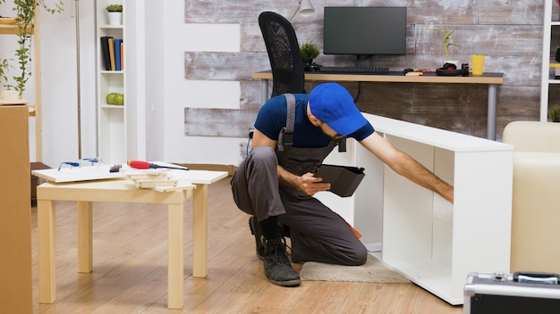 Lavoratore di sesso maschile che utilizza la tecnologia moderna per l'assemblaggio di mobili in una nuova casa. Lavoratore con computer tablet.