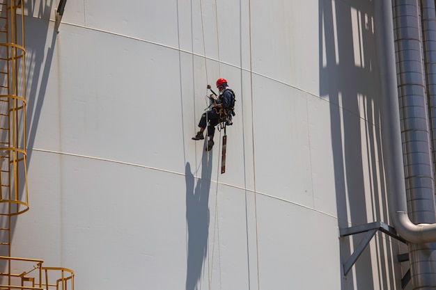 Lavoratore di sesso maschile in basso altezza serbatoio shell piastra scala di corda accesso ispezione di sicurezza del gas propano del serbatoio di stoccaggio di spessore.