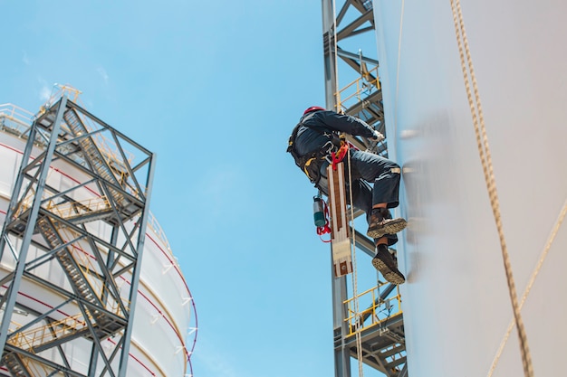 Lavoratore di sesso maschile in basso altezza serbatoio shell piastra scala di corda accesso ispezione di sicurezza del gas propano del serbatoio di stoccaggio di spessore.