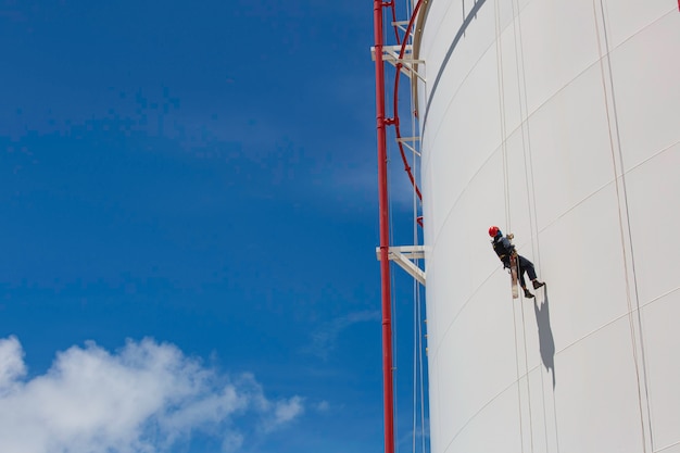 Lavoratore di sesso maschile in basso altezza serbatoio shell piastra scala di corda accesso ispezione di sicurezza del gas propano del serbatoio di stoccaggio di spessore.