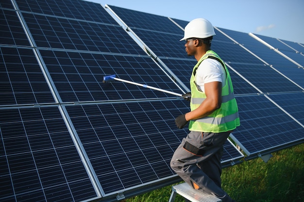 Lavoratore di una centrale elettrica alternativa in uniforme che pulisce i pannelli solari con un mop Un bel afroamericano che si prende cura delle attrezzature