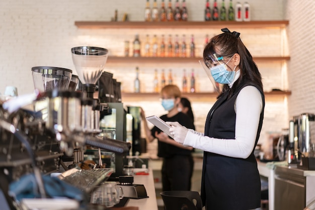 Lavoratore donna asiatica che indossa maschera chirurgica e schermi per il viso presso la caffetteria