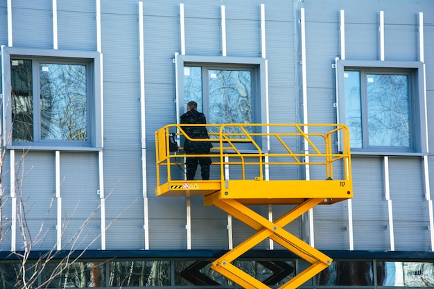 Lavoratore edile che utilizza un ascensore a forbici per installare la cassa di rivestimento dell'edificio