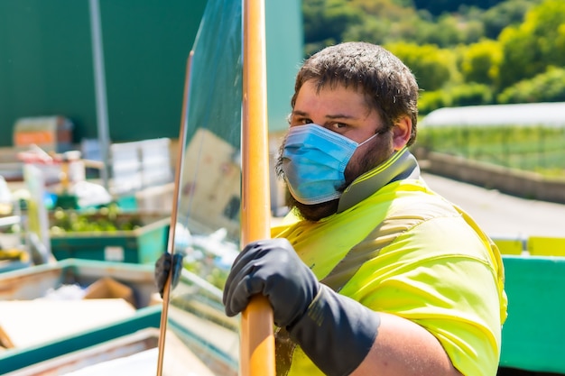 Lavoratore in una fabbrica di riciclaggio o in un punto pulito e immondizia con una maschera facciale e con protezioni di sicurezza. Operatore che pulisce e ordina l'installazione