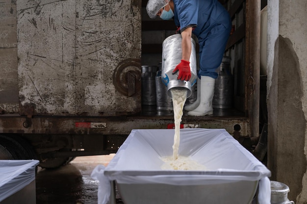 Lavoratore in uniforme che versa il latte in un contenitore in una fabbrica di lavorazione del latte