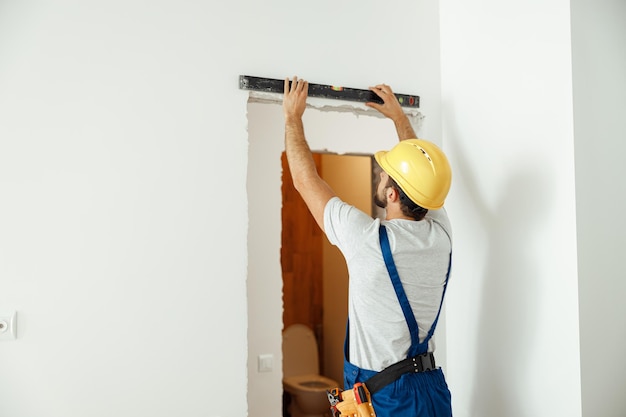 Lavoratore maschio professionista tuttofare in uniforme che usa la livella mentre prende le misure all'interno