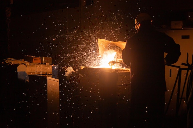 Lavoratore siderurgico che rimuove le scorie dal forno in acciaio con scintille e scarico dei fumi