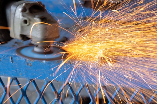 Lavoratore taglio acciaio con rettificatrice e spruzzi di scintille in officina