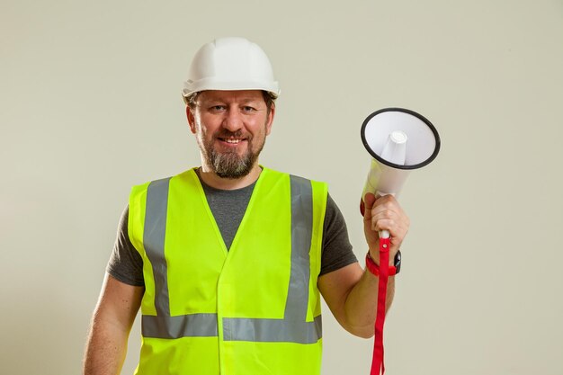 Lavoratore uomo in un giubbotto e un cappello da casco da costruzione bianco con un altoparlante in mano su un bianco