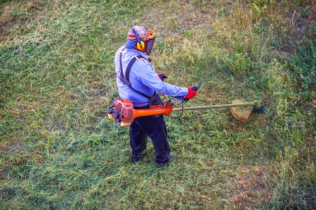 Lavoratore uomo tosaerba vista dall'alto che taglia erba secca con tosaerba