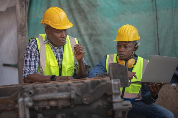 Lavoratori africani Ingegnere che tiene in mano un laptop per il controllo e l'ispezione del motore della macchina pesante