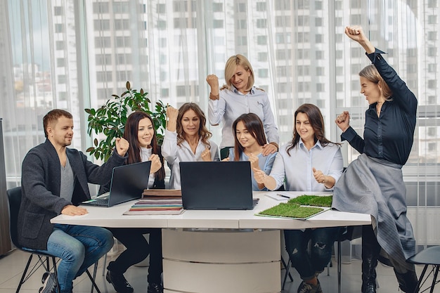 Lavoratori attraenti ed emotivi che hanno appreso la buona notizia sono seduti allo stesso tavolo e sorridenti in ufficio. Buona giornata concetto