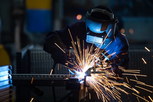 Lavoratori che indossano uniformi industriali e maschera di ferro saldato negli impianti di saldatura dell&#39;acciaio.