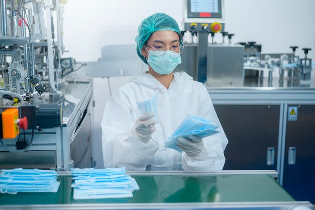 Lavoratori che producono maschera chirurgica in una fabbrica moderna, protezione Covid-19 e concetto medico.