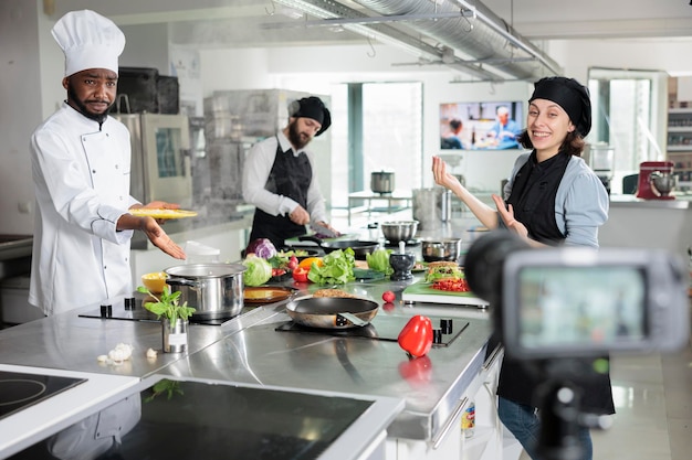 Lavoratori dell'industria alimentare che girano video per programmi di cucina televisiva mentre creano piatti gourmet da cucina raffinata. Gli chef nella cucina del ristorante registrano il processo di preparazione del pasto per il corso su Internet.