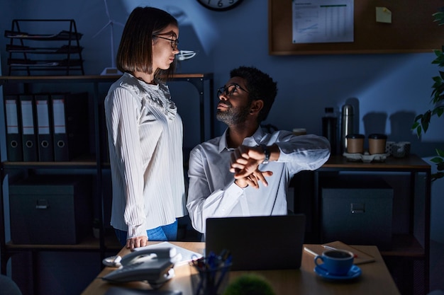 Lavoratori di affari dell'uomo e della donna che utilizzano il computer portatile che guarda l'orologio all'ufficio