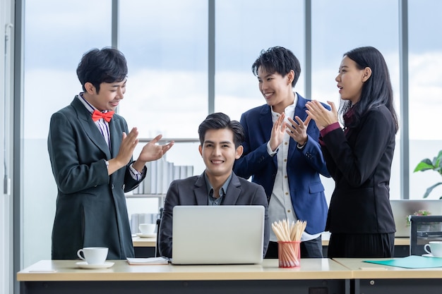 Lavoratori felici di successo Gruppo di uomini d'affari asiatici con generi diversi (LGBT) Battere le mani e congratularsi con l'uomo d'affari vedere un business plan di successo sul computer portatile nella sala riunioni